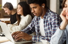 Diversos alunos estudando juntos com laptops e fones de ouvido em um ambiente de trabalho bem iluminado.
